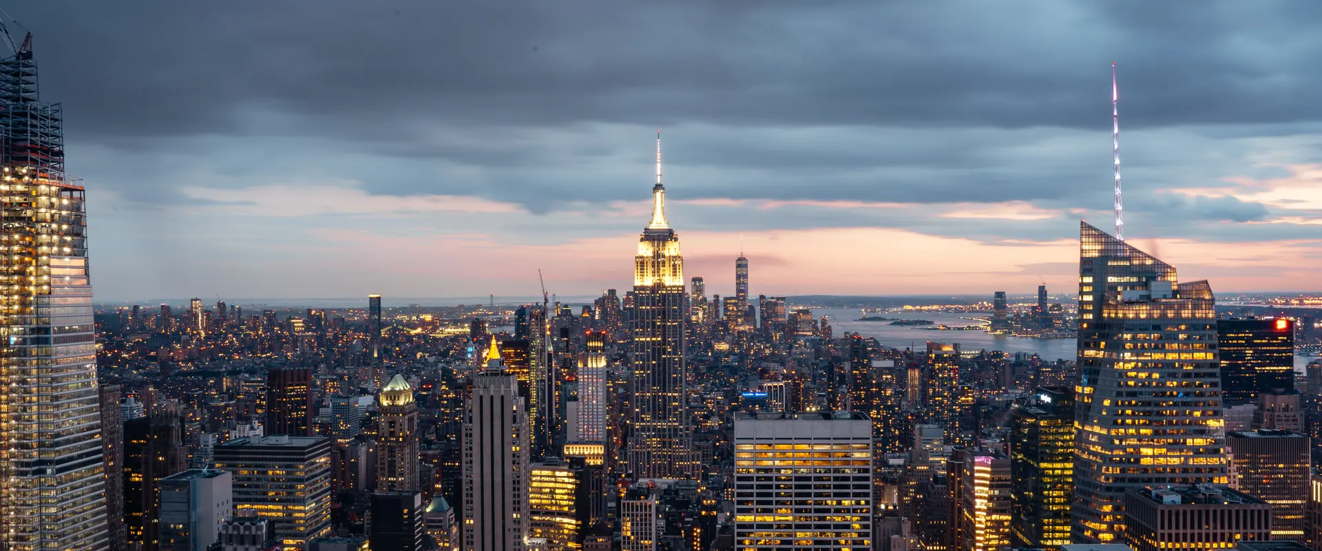 Midtown Manhattan at dusk, the lit Empire State Building against cloud with lower Manhattan and the harbour beyond